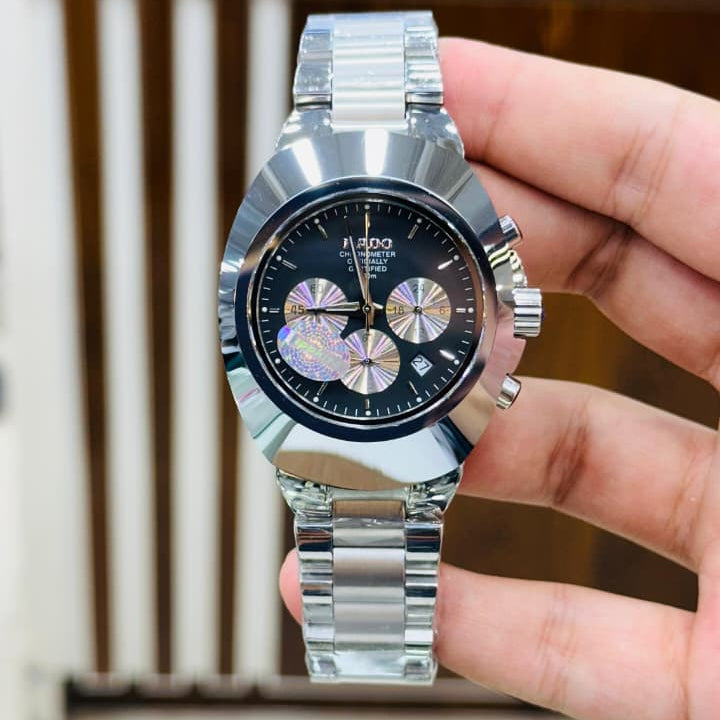 Hand holding a silver watch with a black face against a blurred indoor background